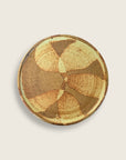 A round ceramic plate with a textured, hand-painted abstract pattern in earthy brown, tan, and cream tones, shown from a top-down view on a light beige background.