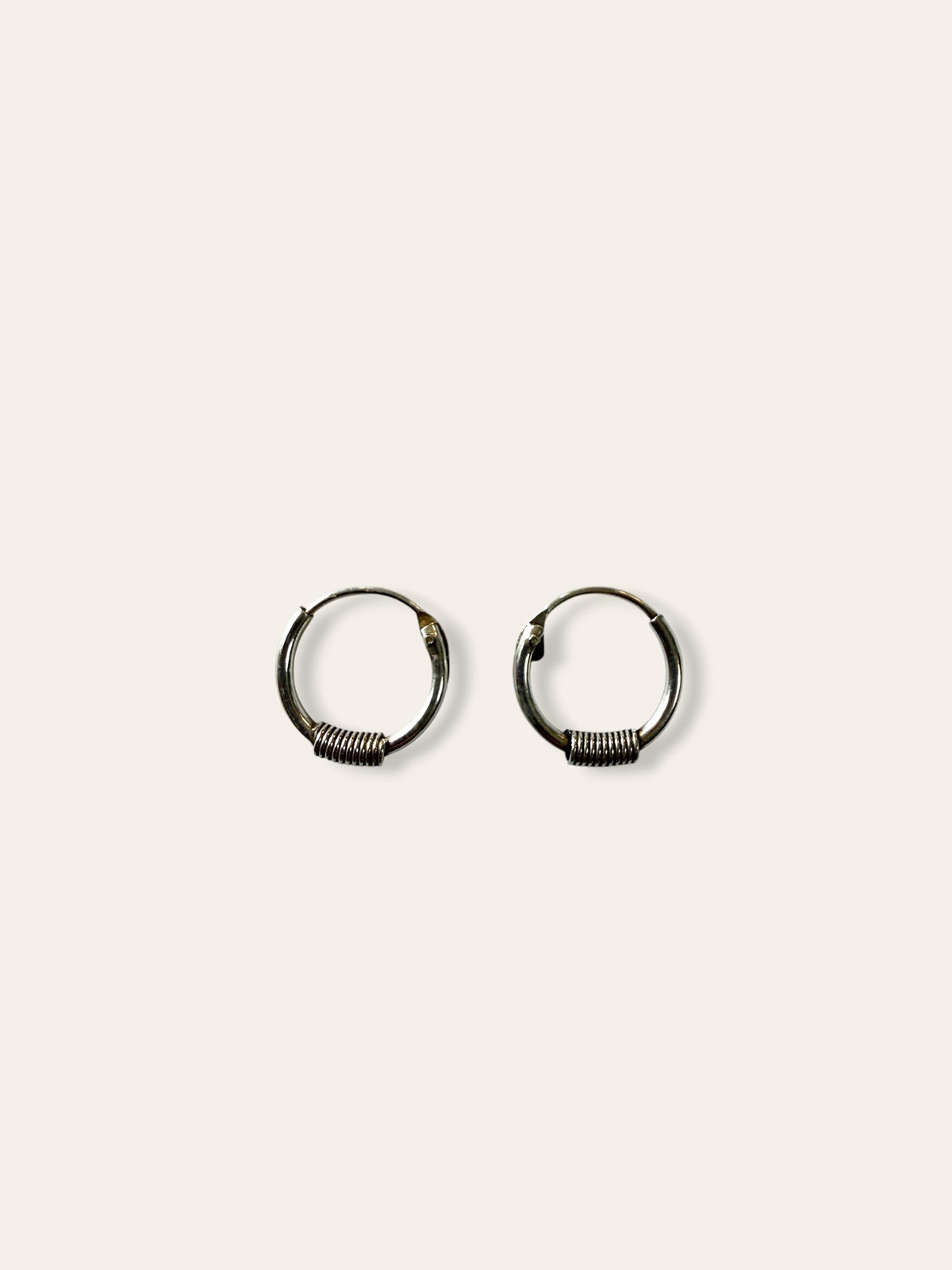 A pair of small silver hoop earrings with textured, ribbed detailing along the lower half, displayed on a solid off-white background.