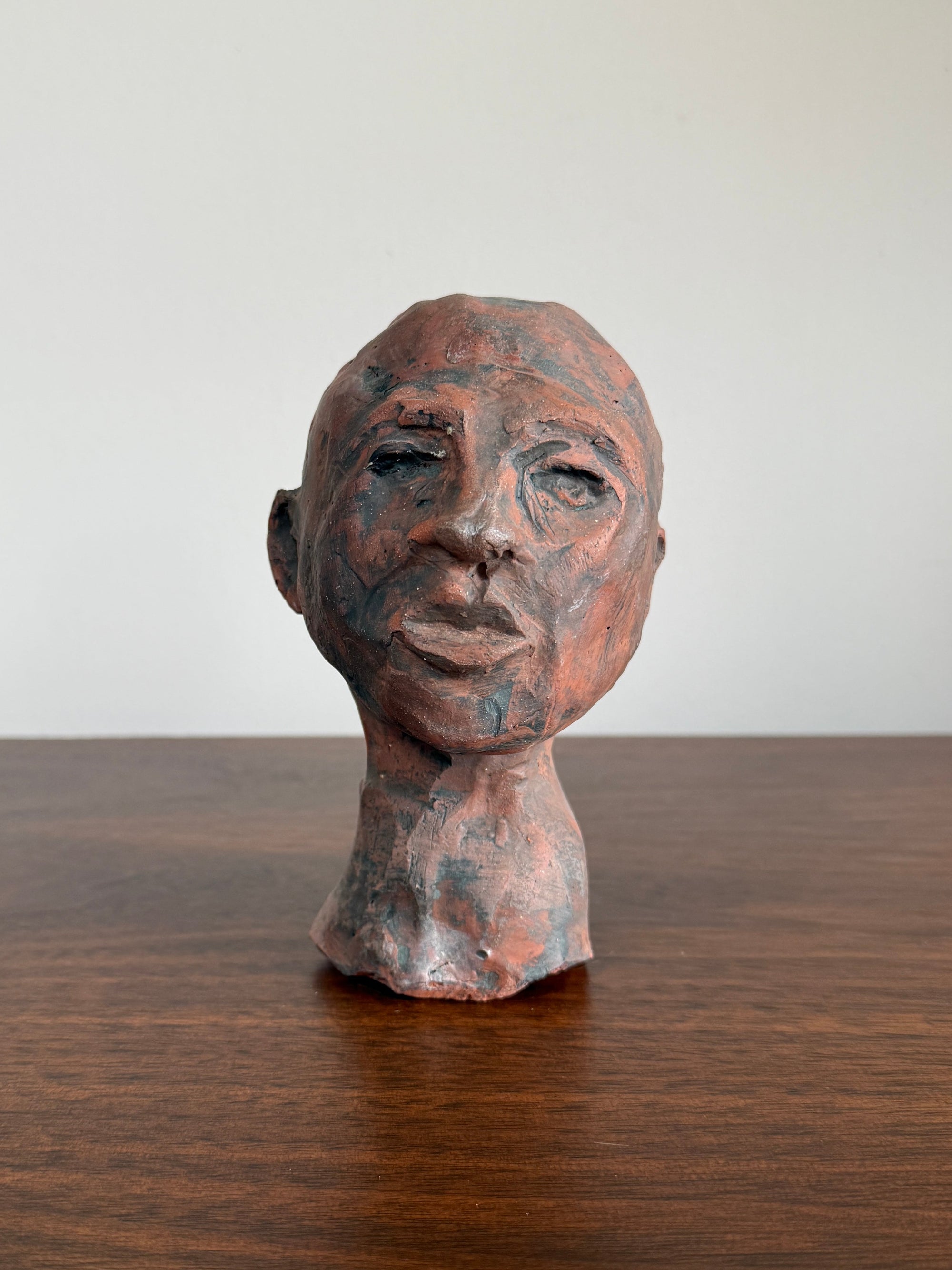 Ceramic sculpture of a human head on a clay surface with a white background