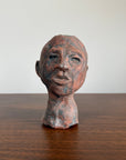 Ceramic sculpture of a human head on a clay surface with a white background